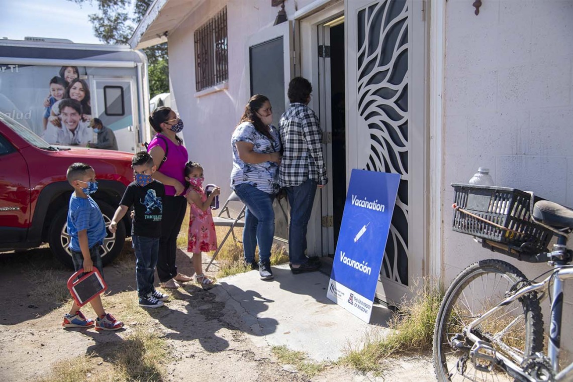 People gather outside a community center for a MOVE-UP clinic hosted by the UArizona Health Sciences in the rural town of Aguila, Ariz., to get COVID-19 vaccine shots. The mobile health unit van of the UArizona Zuckerman College of Public Health is visible in background.