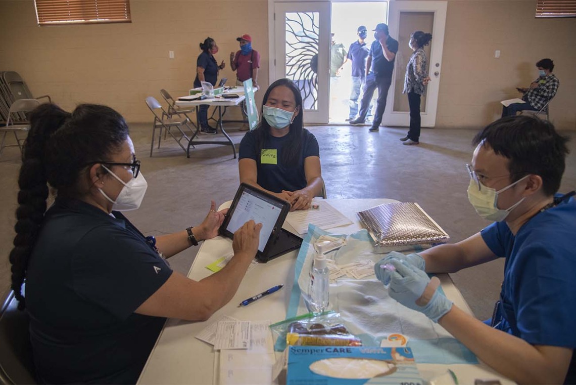 Maria Jaime, a health educator with the College of Public Health in Phoenix, goes through a patient’s answers on her registration, while vaccinator Alvin Wong, DO, an internal medicine physician with the UArizona College of Medicine – Phoenix, prepares the vaccine.