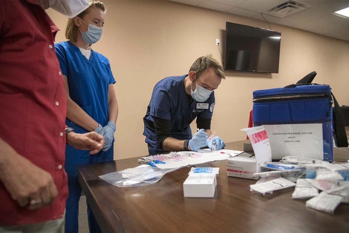 College of Nursing student Graham Robinson gets instruction on how to measure an appropriate dosage of the COVID-19 vaccine to be administered to patients at a MOVE UP clinic at the Consulate of Mexico in Douglas in partnership with the UArizona Health Sciences  and Cochise County Health Department. Fellow Nursing student Jane Leahy is to left of him.