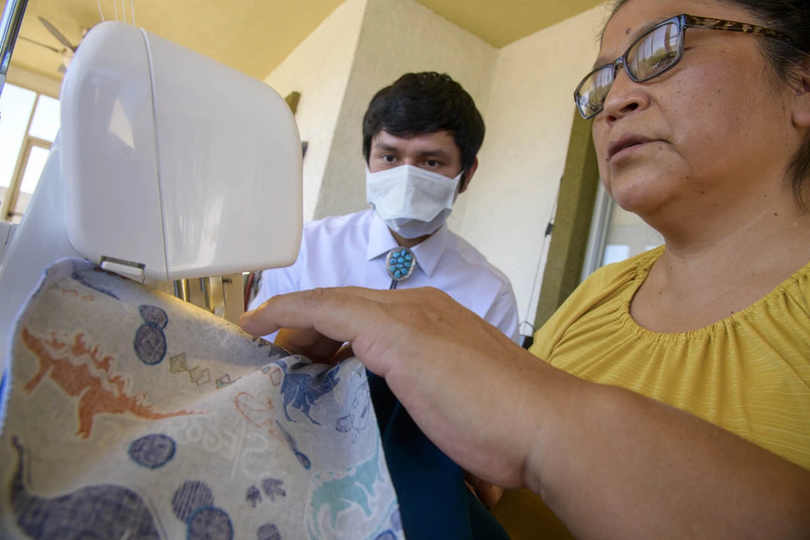 University of Arizona College of Medicine – Tucson student Aaron Bia watches as Navajo seamstress Theresa Hatathlie-Delmar sews a surgical cap with material donated in the college’s PPE drive.