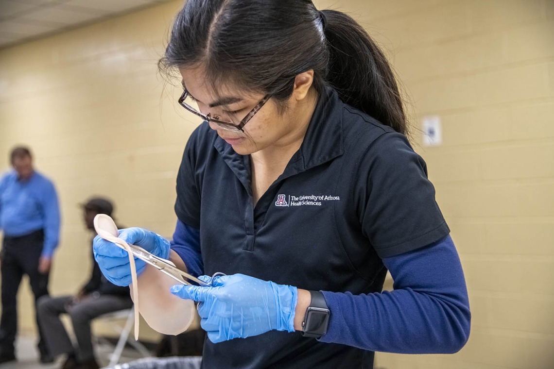 Merryl Lopido, simulation operations specialist for ASTEC, cuts synthetic skin to be placed on a volunteer to simulate a realistic-looking wound.