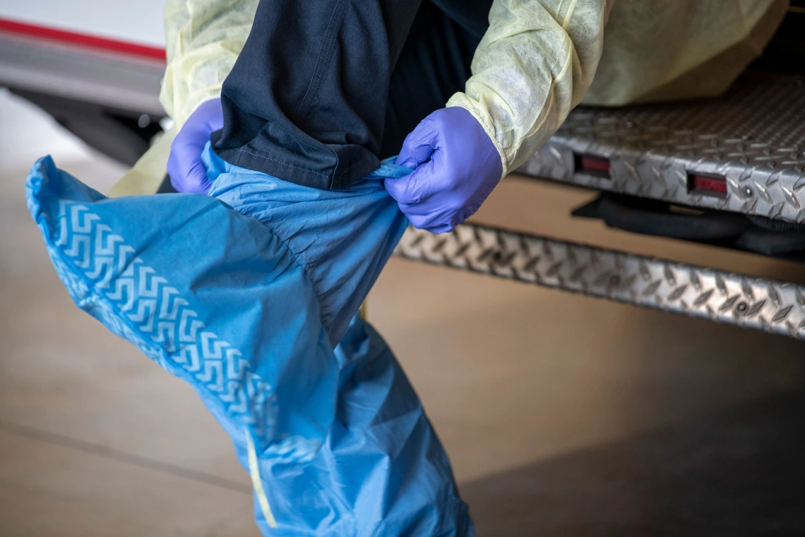 Tucson Fire Department’s Taylor Parrish puts on a protective gown and boot coverings to prevent spread of disease before entering the home a possible COVID-19 patient.