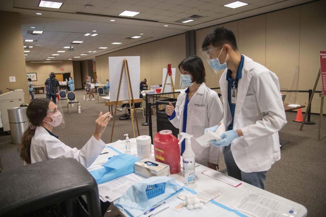 College of Pharmacy students Catherine Hensley (left) and Sang Nguyen (right) consult preceptor Eva Liang, PharmD (center), about techniques for administering a shot.