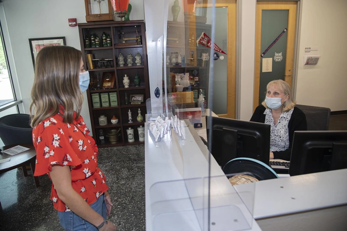 Newly installed plastic barriers protect staff and visitors in a reception area in Drachman Hall. From left: Ali Bridges, College of Pharmacy director of communication, and administrative assistant Amy Dorgan.