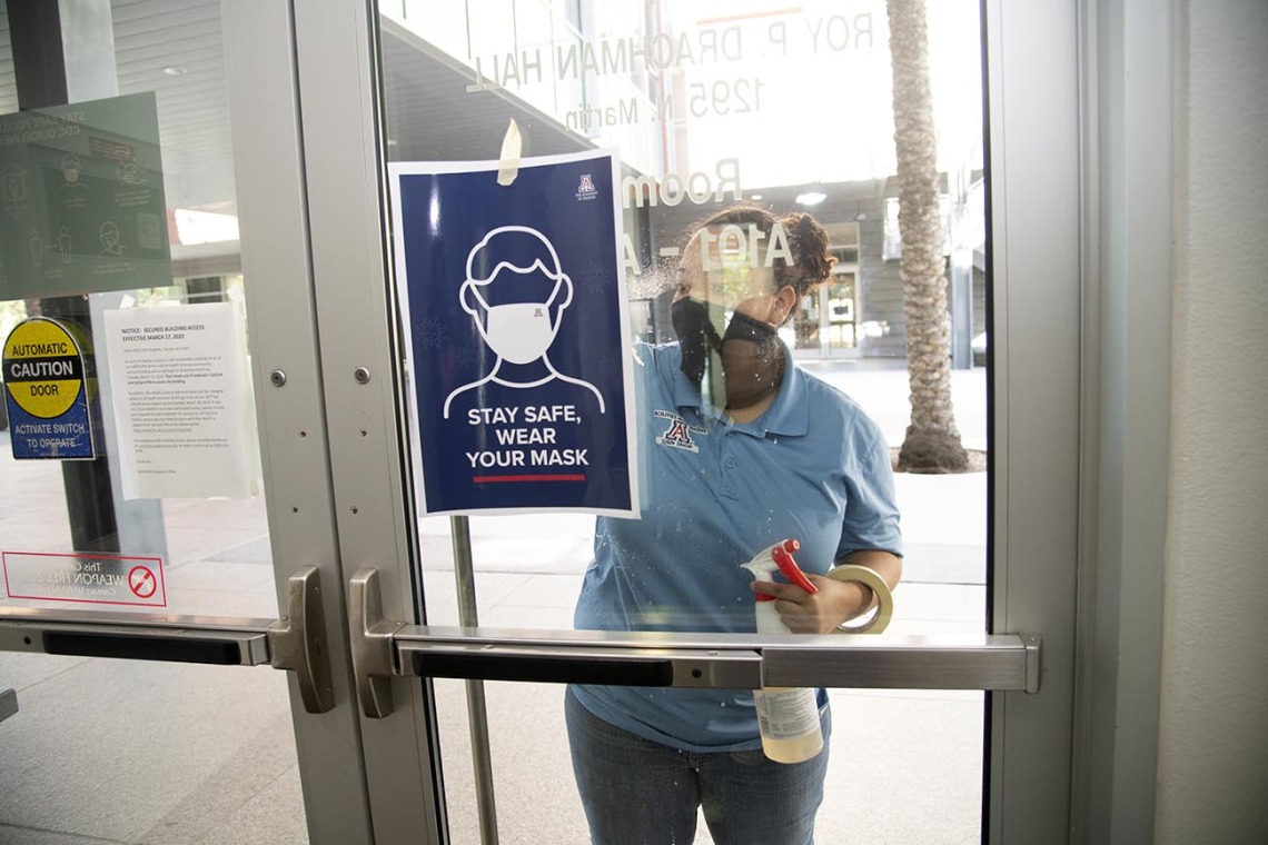 Alexandra Almli from University of Arizona Facilities Management cleans a door at the Mel and Enid Zuckerman College of Public Health before placing new signage.