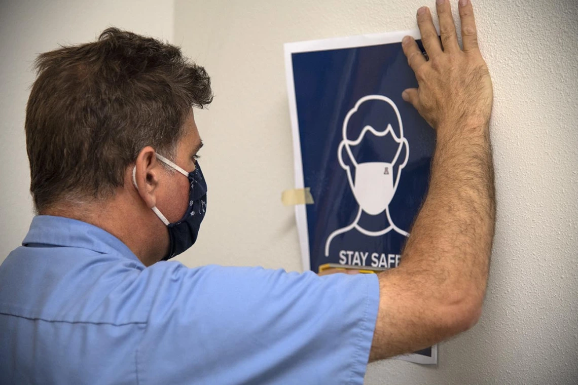 Chris Skertic from University of Arizona Facilities Management hangs new signage that reminds everyone to wear masks and maintain appropriate physical distance.