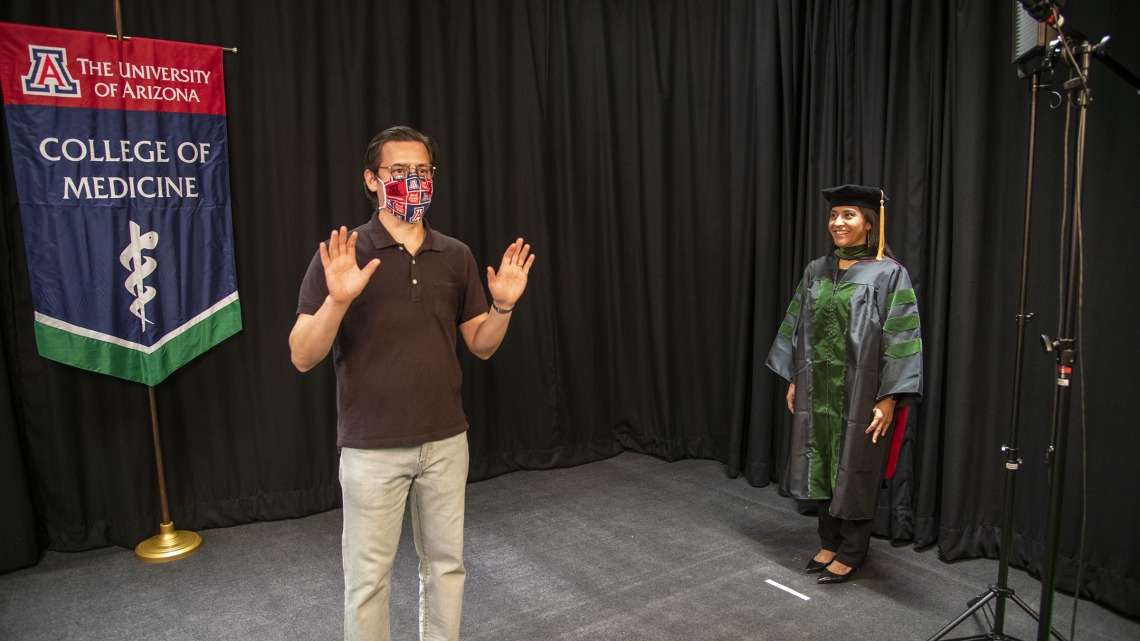 Gilberto Vega shows medical student Cazandra Zaragoza how to simulate walking across a stage on graduation day. College of Medicine – Tucson student photos and videos will be used in the college’s virtual convocation event.