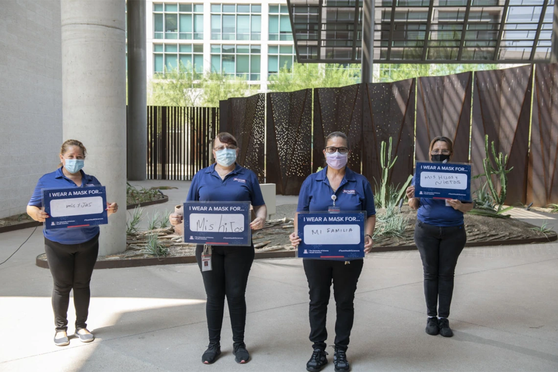 Alicia Espinoza, Bertha Chavez, Sandra Romo and Altagracia Coronado, who provide building services for the Phoenix Biomedical Campus, hold their signs in a courtyard.