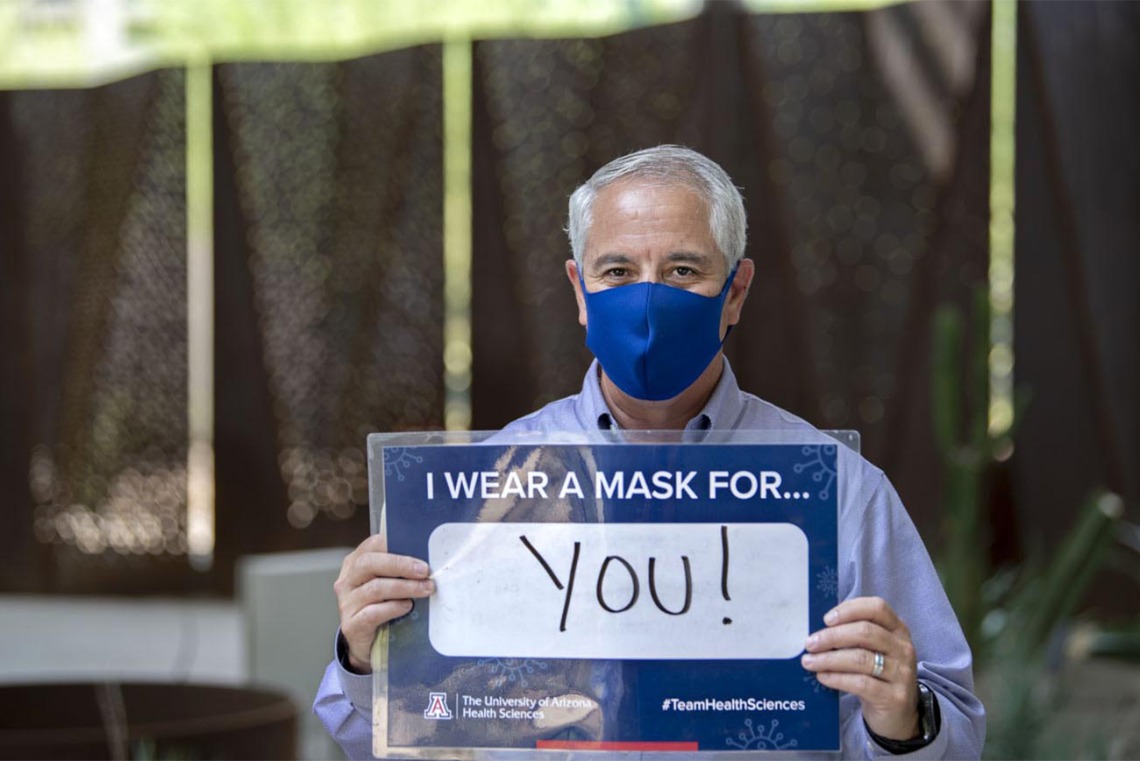 Tony Malaj, executive director of campus management and operations of UArizona’s Phoenix Biomedical Campus, holds a sign that reads, “I wear a mask for you!”