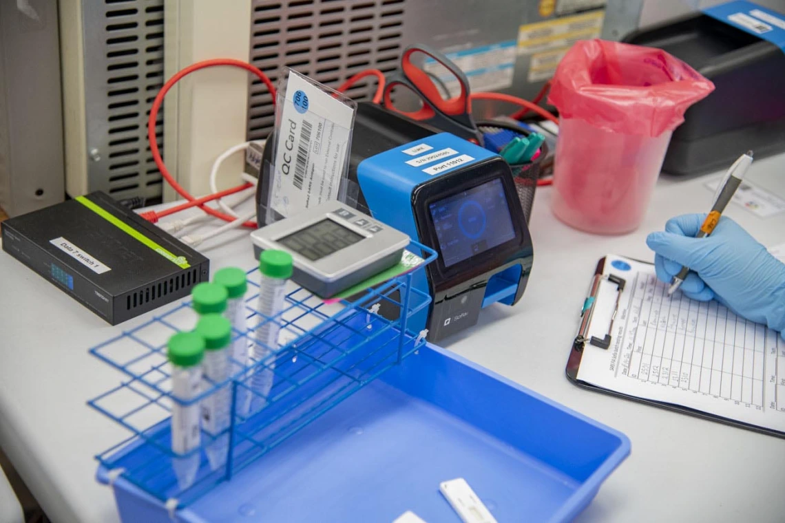 Lab tech Jennifer Alvarado places a cassette with a person's nasal swab sample into the machine that will process it and determine whether the person is positive or negative for COVID-19. This blue machine takes 11 seconds to produce a result, and a person is notified of their results via email within two hours of taking the test.