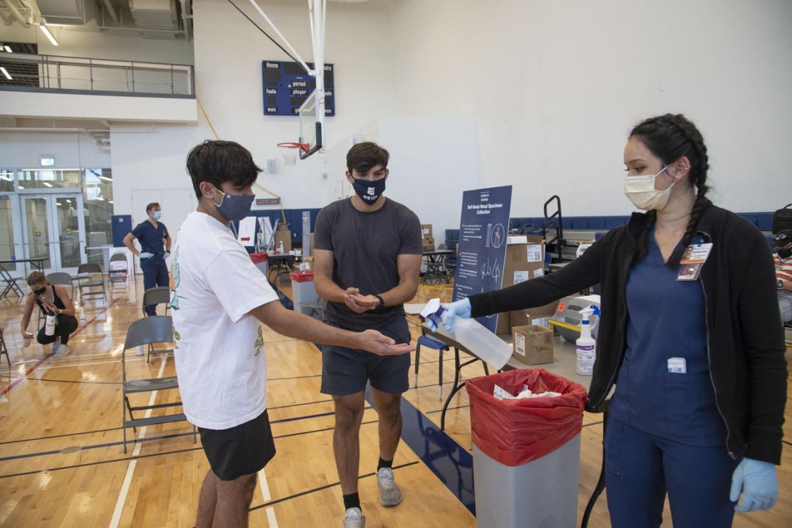 Clinical research coordinator Brenna Abril provides sanitizer spray for students Mason Young and Heath Zuniga after they take an antigen test at the University of Arizona Recreation and Wellness Center, known as NorthREC, in Tucson.
