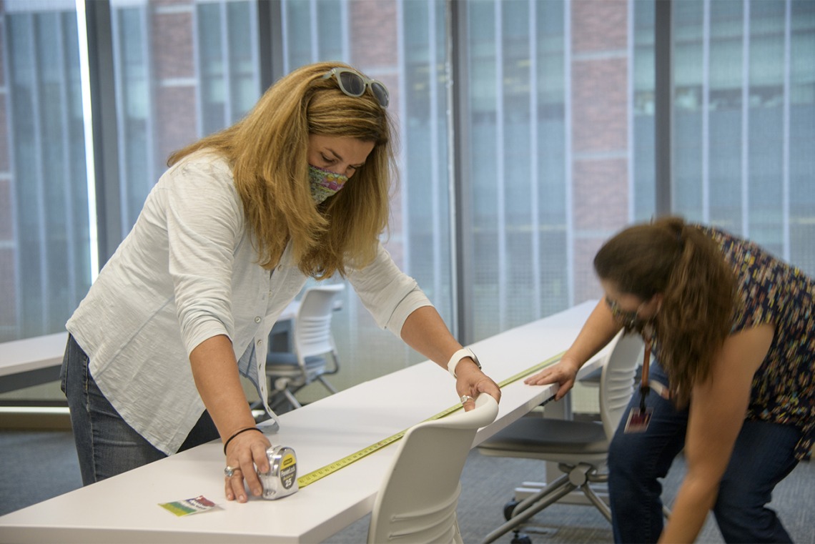 Angie Souza (left) and Jill Garcia (right) of Health Sciences Planning and Facilities measure the distance between desks in the Health Sciences Innovation Building to calculate new seating requirements, ensuring people stay six feet apart.