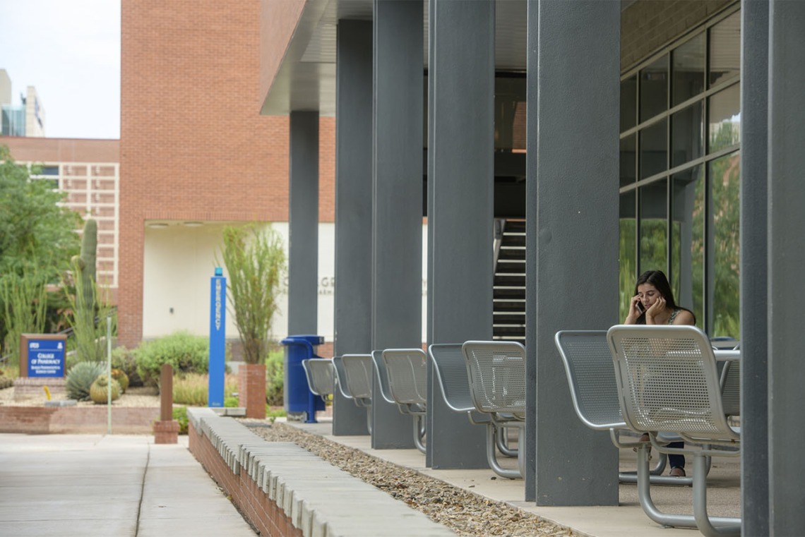 The western porch along the ground-floor of Drachman Hall has several tables and chairs tucked in the shade of the building. You have a good view of the busy bike- and pedestrian-ways that pass through the Tucson campus from here. 