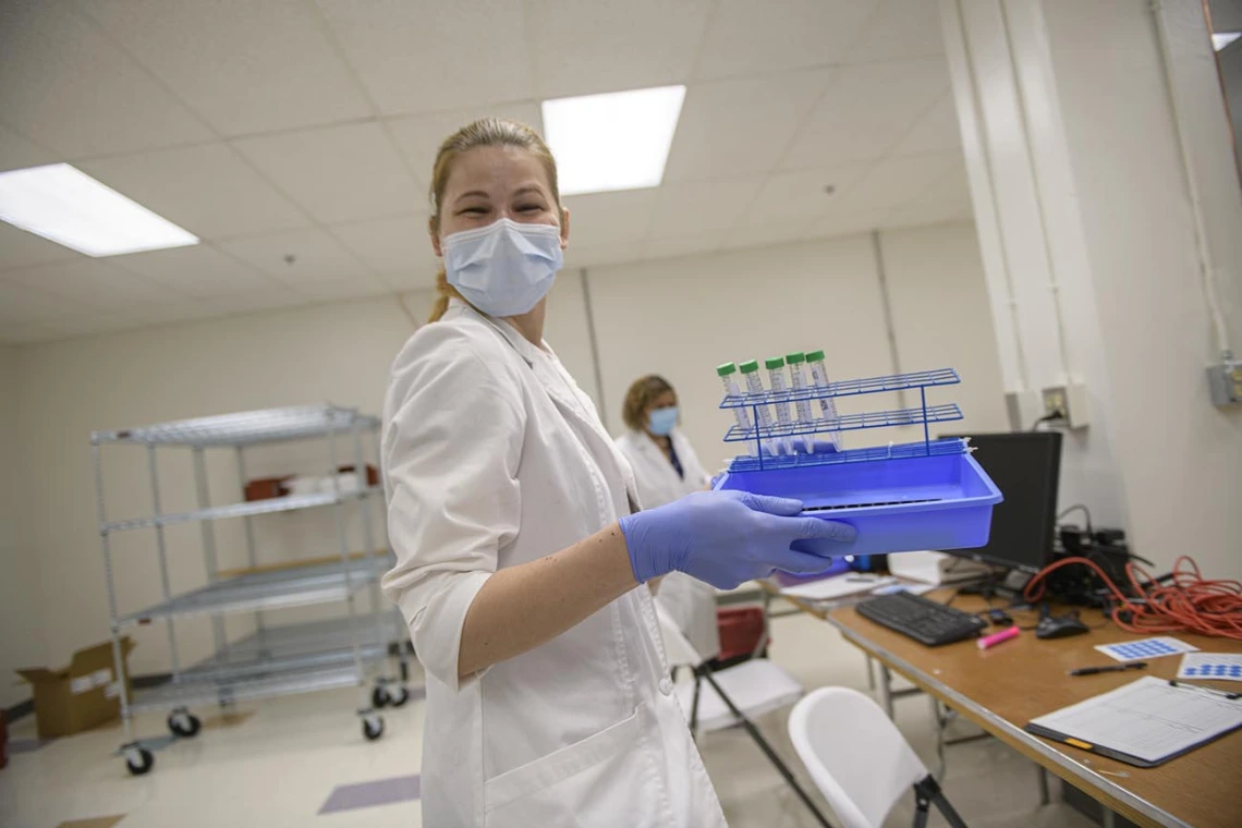 Anete Milkovica, a research technician, carries a set of nasal swab samples to a lab technician to start processing the tests. 