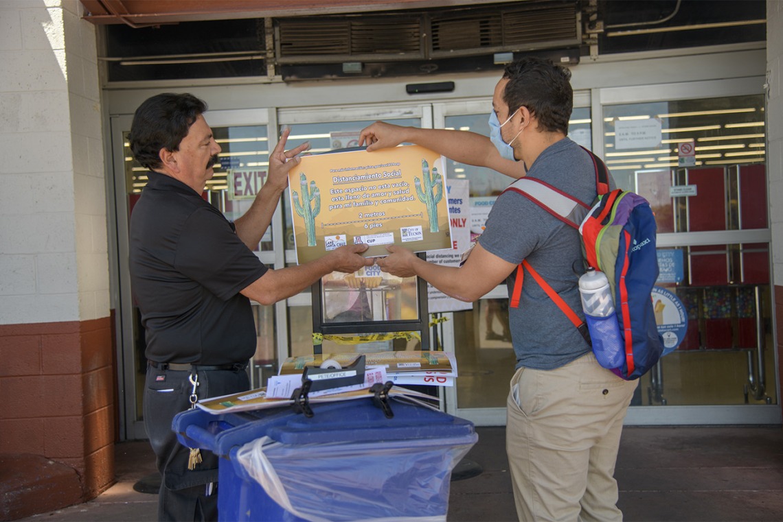 Assistant Store Manager Peter Ramirez and fourth-year medical student Ricardo Reyes hang a social distancing sign outside a Food City grocery store on South Sixth Avenue in Tucson as part of an outreach campaign about social distancing.