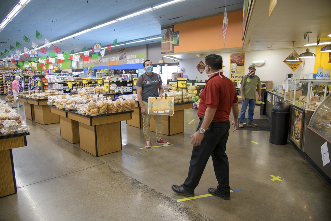 Fourth-year medical student Ricardo Reyes joins Food City Store Manager Ramon Lopez show what social distancing looks like at the store on West Ajo Way by staying six feet apart, using the lines on the floor of the grocery store as guides.