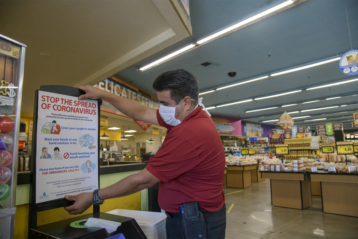 Store Manager Ramon Lopez hangs a “stop the spread poster” from the Pima County Health Department at the Food City grocery store on West Ajo Way.