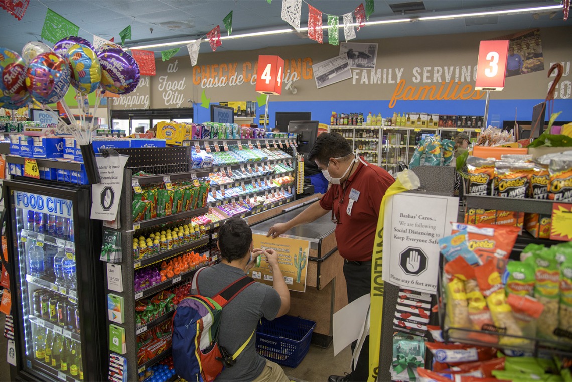 Fourth-year medical student Ricardo Reyes and Store Manager Ramon Lopez hang a social distancing poster at the end of a grocery check-out aisle at a Food City grocery store on West Ajo Way in Tucson.