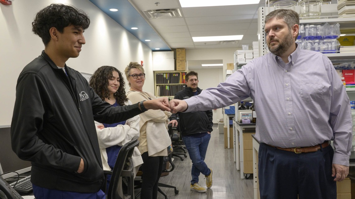 Esteban Ramirez, a student from Pima County JTED, a technical education program for high school students, bumps fists with Nathan Cherrington, PhD (right), director of the Southwest Environmental Health Sciences Center, at a January tour of his lab in the R. Ken Coit College of Pharmacy. 