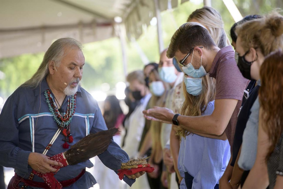 During the smudging ceremony, Dr. Carlos Gonzales holds the shell containing the burning herbs for a student to pull the smoke over himself as part of the blessing. 
