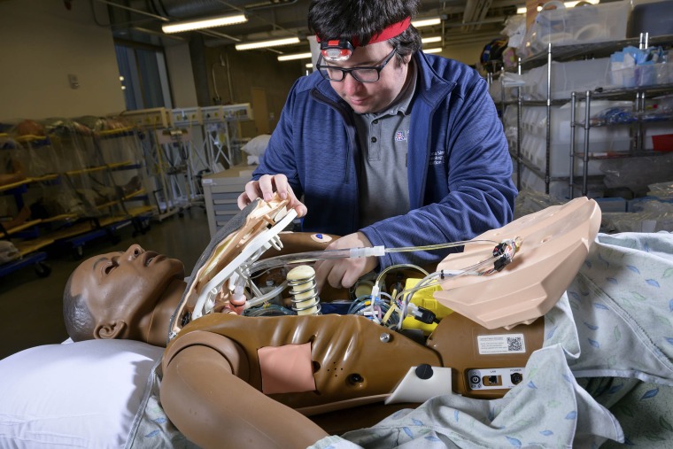 Lucas Grijalva reaches inside a simulation manikin to check on its interior parts. 
