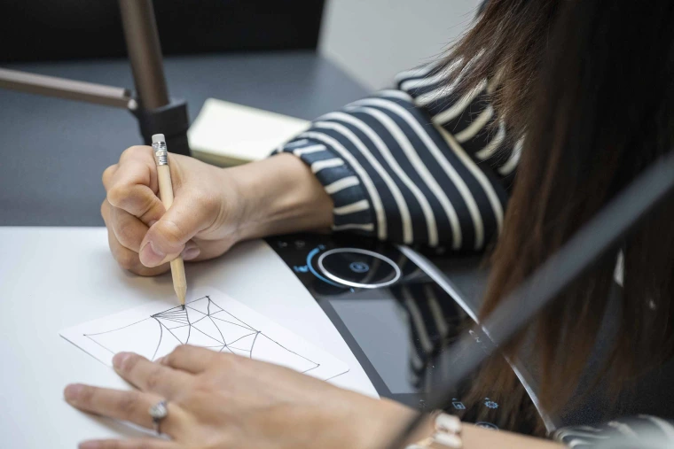 Close-up photo of a hand gripping a pencil, doodling on paper.