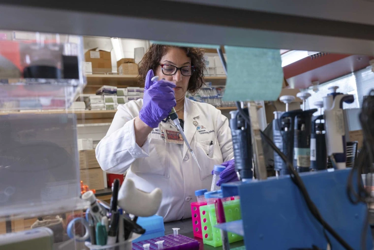 Fariba Donovan, MD, PhD, holds a pipette in a gloved hand in a lab at the University of Arizona Valley Fever Center for Excellence.