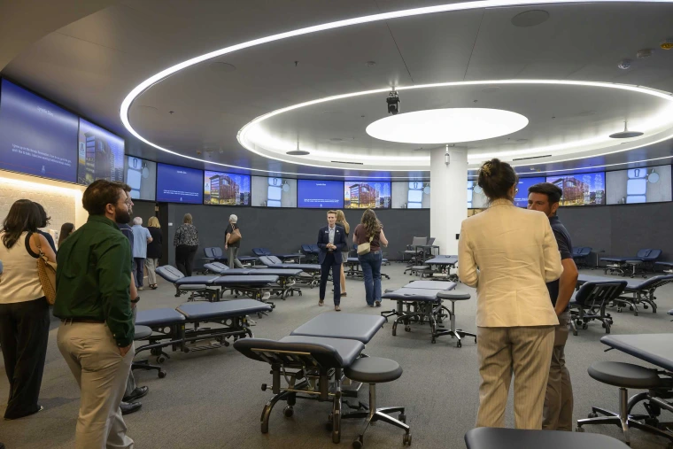 Photo of several people chatting together in a circular room filled with examining tables in the new lab space of the University of Arizona School of Health Professions Physical Therapy and Physician Assistant studios.