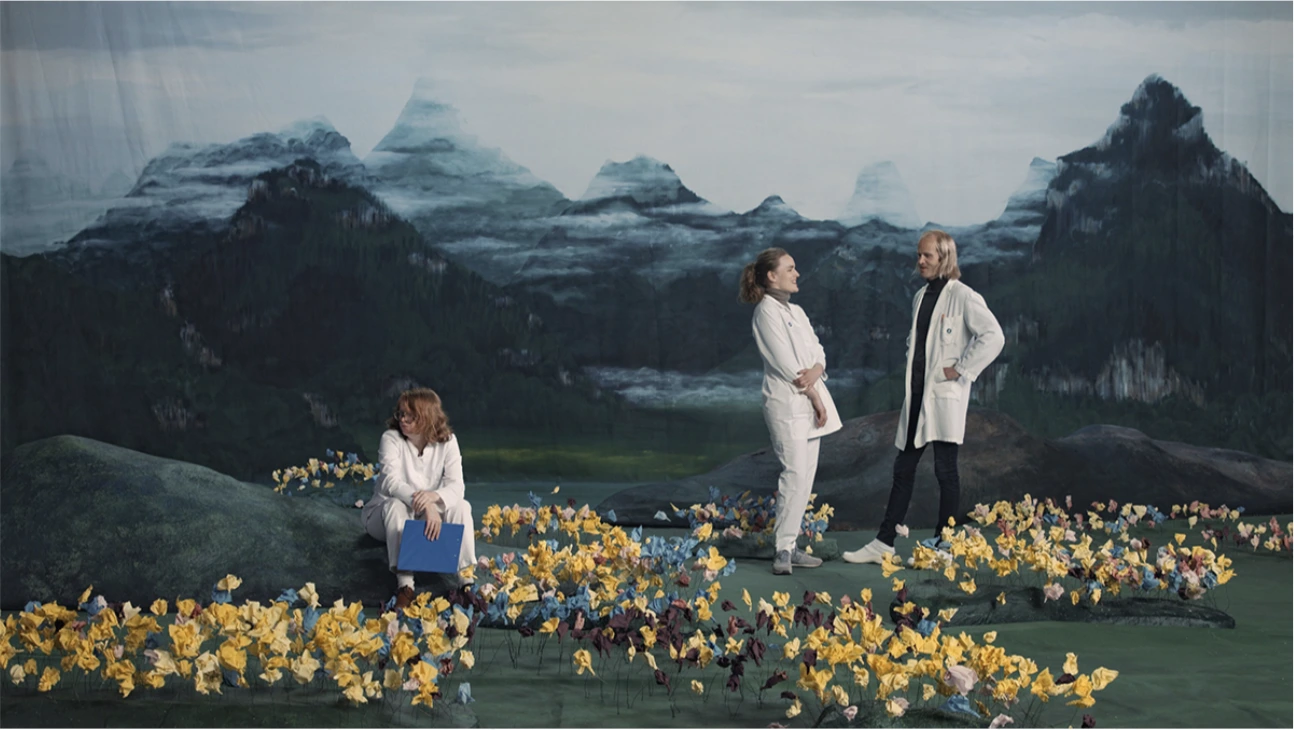 Teaser of Ragnar Kjartansson's "Figures in Landscape", three doctors in white coats in a field of artificial flowers