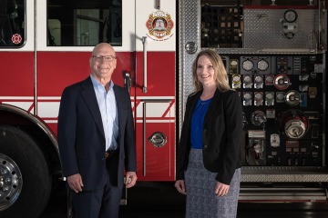 Man and woman standing in front of a fire truck.