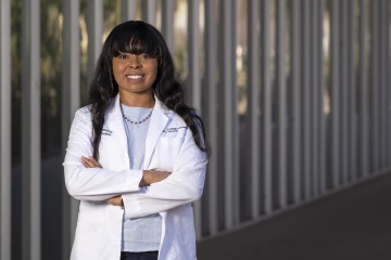 Black woman in doctor's white coat stands with arms crossed