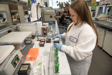 Woman wearing a white lab coat working at a lab bench.
