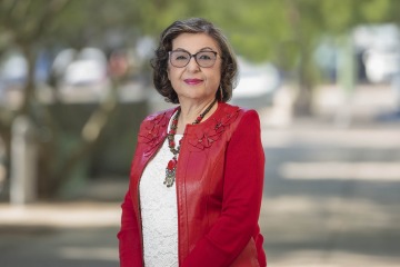Woman wearing a red jacket, white blouse and glasses stands outside.