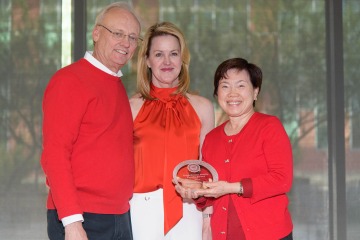 A tall man and woman stand with another women holding a glass College of Pharmacy award. All are wearing red. 