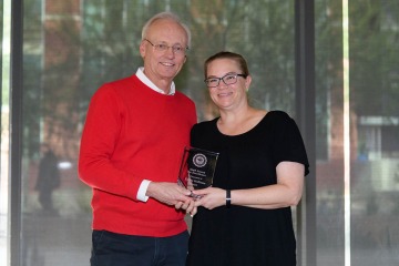 Tall man in red sweater standing with woman in black dress holding glass Pharmacy award.