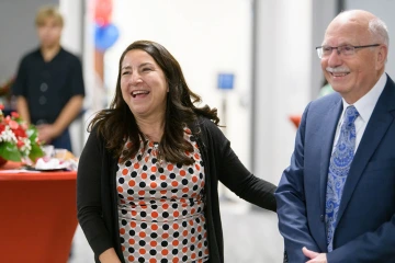 A woman with long dark hair laughs as he holds the arm of older bald man in a suite who is also smiling. 