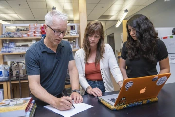 man writing on a piece of paper with two women looking over his shoulder