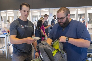 Two men in a medical symulation setting fill a backpack full of items to donate to homeless veterans. 