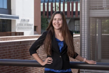 Portrait of a woman with long brown hair standing in front of the R. Ken Coit College of Pharmacy