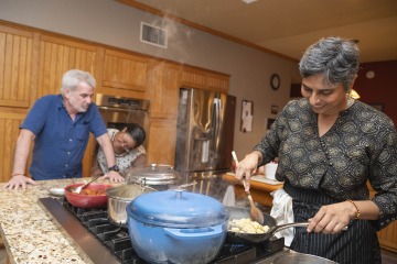 Woman cooking in a kitchen. She has multiple pots going at once and her husband and daughter are watching her cook.