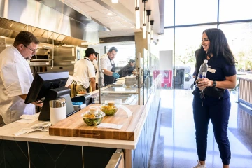 Woman waits for her food to be prepared as three chefs work in the open kitchen at Cafe Bolo.