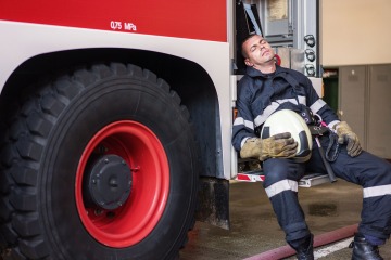A firefighter rests on a fire truck.