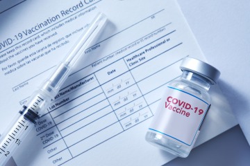 Stock image of vaccine syringe and bottle on top of immunization paperwork