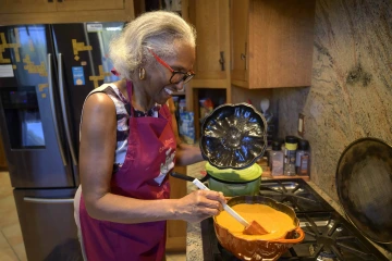 Woman stirs a pot on a stove in a kitchen.