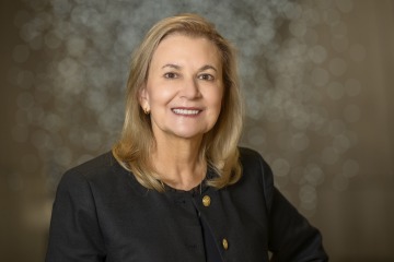 Woman with shoulder-length blonde hair wearing a black suit jacket.