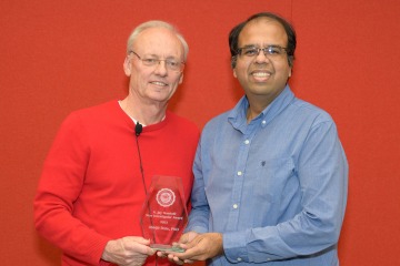 Two men stand next to each other holding a glass award between them, both smiling. 