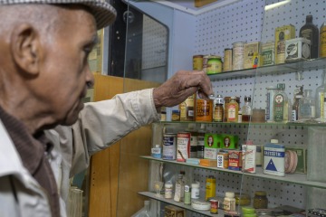 Charles Kendrick holds his hand above shelves filled with bottles of medications that are part of his collection of artifacts from the Black history museum he started. 