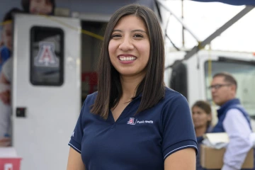 Sheila Soto stands in front of a mobile health truck and a display for the UArizona Mel and Enid Zuckerman College of Public Health display.