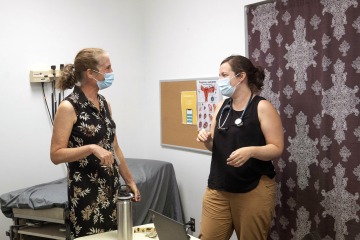 Two women in masks talk in an exam room at Casa Alitas.