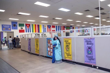 A room with flags of many nations on the wall. At the front is a replica statue of the Statue of Liberty holding a baby.